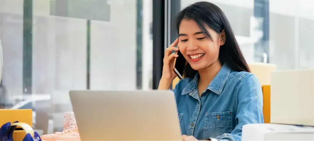 A small-business owner smiling during a phone call while working at her laptop.