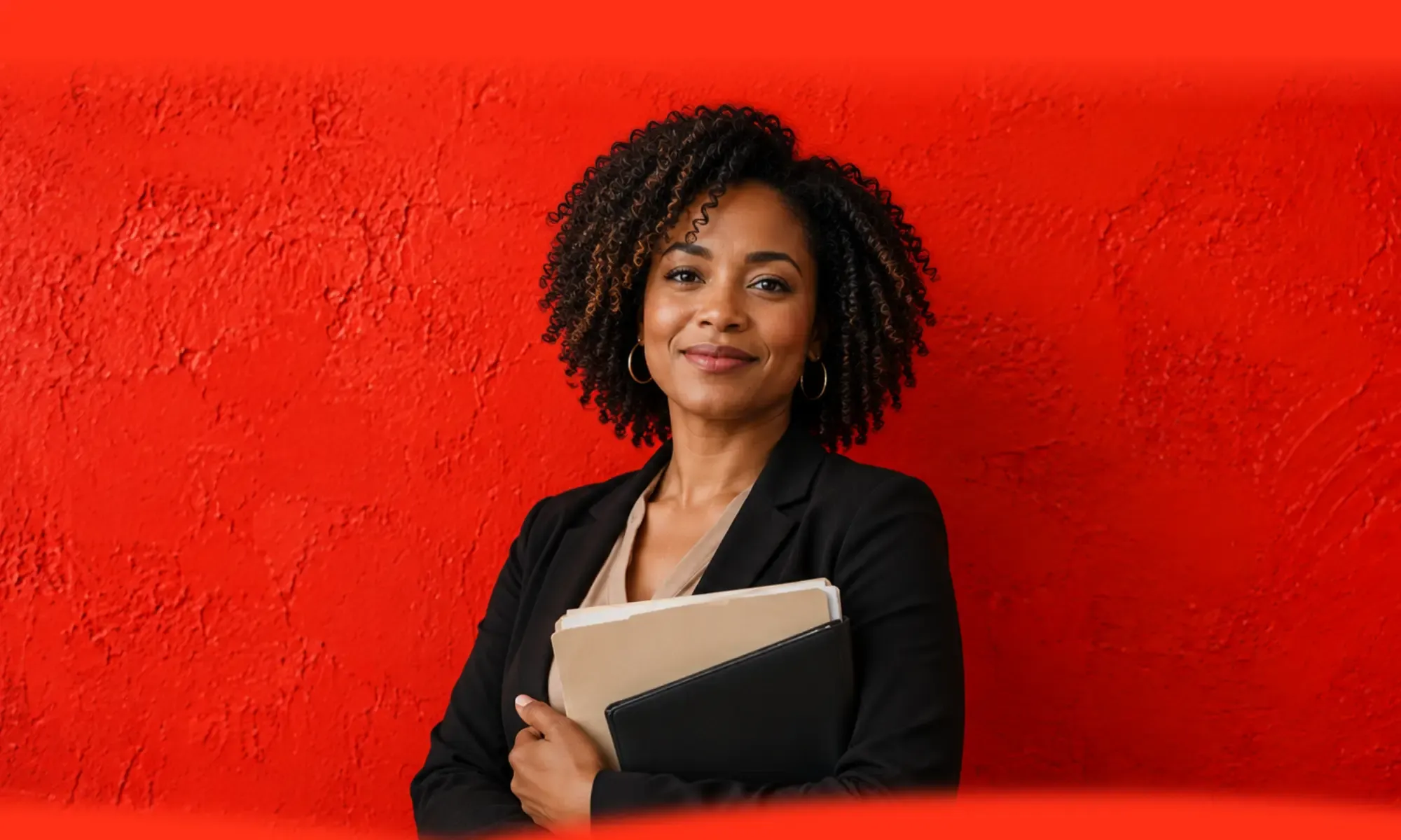 A confident non-profit leader in a black blazer holding folders against a bold red wall